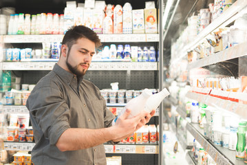 Adult man in a supermarket with a bottle of milk in his hands. Buyer selects milk in the milk...