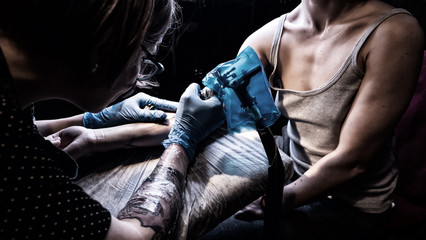 Fototapeta na wymiar Tattoo artist make tattoo in studio, tattooing on the body. Floral tattoo