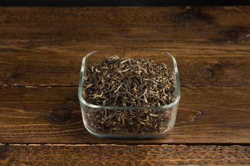 dry green tea in the transparent bowl isolated on wooden table on black background