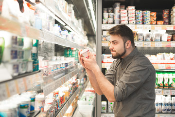 Funny man with a beard is in the milk department of the supermarket near the shelves of...