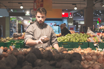 Man in mittens selects vegetables in a supermarket. Adult man digging ingredients for dishes at a grocery store, a vegetable department. Buyer buys vegetables.