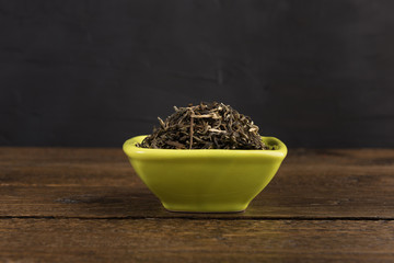dry green tea in a clay bowl isolated on wooden table on black background