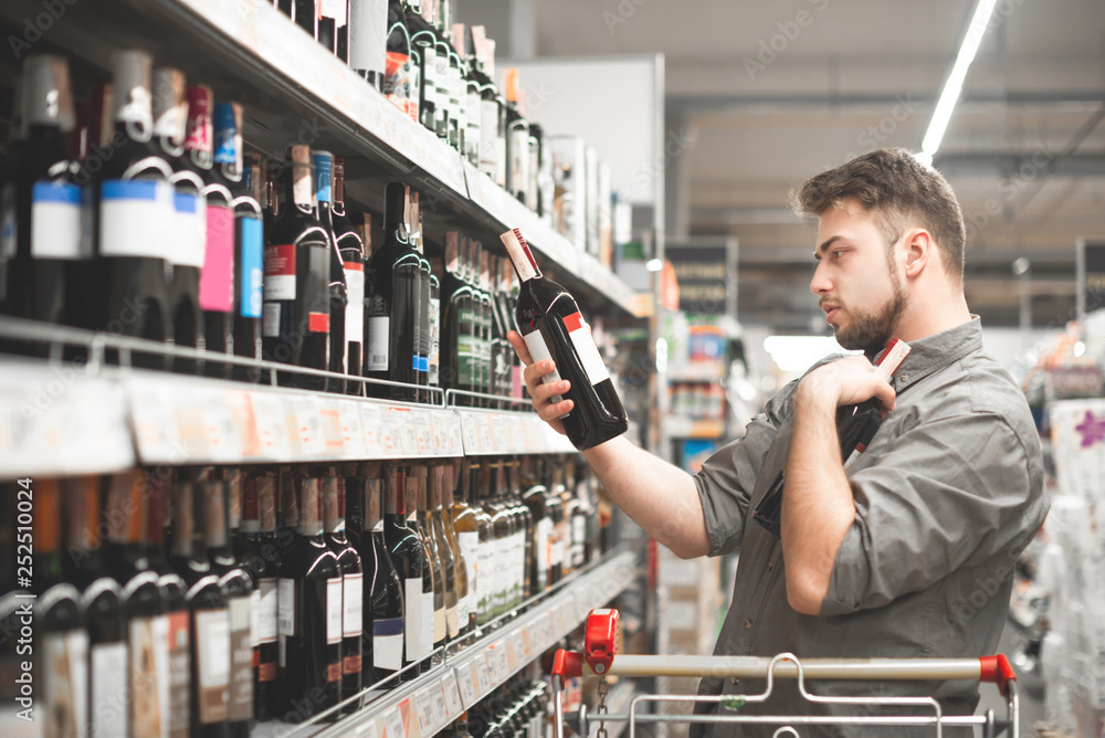 Wall mural this should be fine. side view of handsome young man holding bottle of wine and looking at it while 