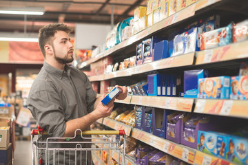 Man stands in a supermarket with a bundle of biscuits in his hands and looks at the shelf with sweets. The buyer buys cookies in a supermarket, looking at packaging with sweet