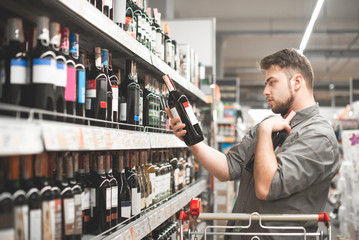 This should be fine. Side view of handsome young man holding bottle of wine and looking at it while...
