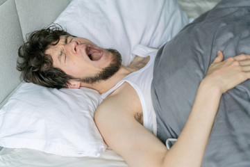 Obraz na płótnie Canvas Cute handsome young man sleeping on bed yawning.