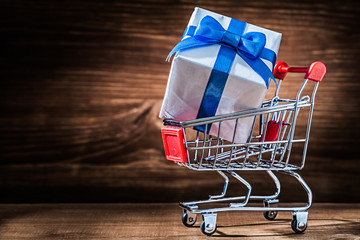 little white giftbox with blue tape in shopping cart on vintage wood