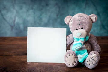 Gray Teddy bear with a blue striped scarf and a postcard on a blue background.