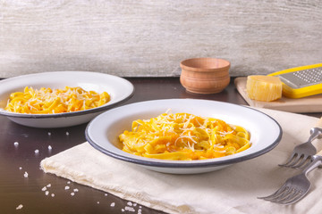 Pumpkin tagliatelle pasta with pumpkin cream parmesan cheese in white plate on dark background