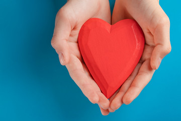 Obraz premium Hands of a teenager child holding a red wooden heart in their hands. Blue background