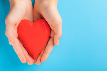 Hands of a teenager child holding a red wooden heart in their hands. Blue background