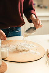 Woman holding scoop and sifting flour on the dough