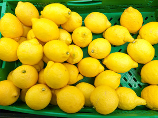 plastic green box at the market plenty of heap yellow lemons ready to be sold to customers.