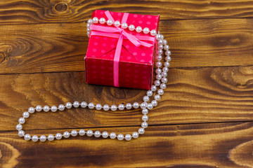 Gift box and pearl necklace on wooden background