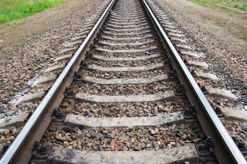 Fototapeta premium Rusty railroad with concrete ties in the forest under grey cloudy sky. Selective focus.