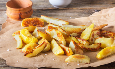 Crisp golden deep fried, french fries hot potatoes, frying and ready to be eaten, really yummy.Potatoes on craft paper on a rustic wooden background