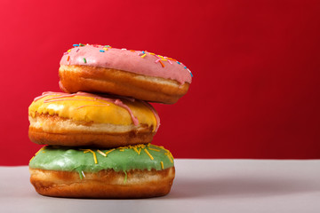 Donuts in multi-colored glaze stacked on top of each other on a red background, copy space. Bakery advertising concept