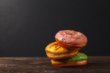 Three colorful donuts on a wooden table, on a black background. Bakery menu design concept. Hanukkah background.