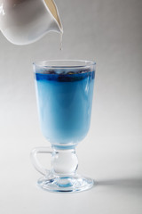 Pour the milk into a Cup of blue butterfly pea tea Anchan on a gray background. Blue Thai tea and milk mixed