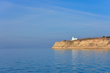 White small lighthouse on cliff by blue Greek sea