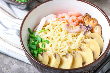 Asian wheat noodles with seafood, pickled mushrooms and scallions, sprinkled with sesame seeds in a bowl on a gray background. Asian style, Japanese food