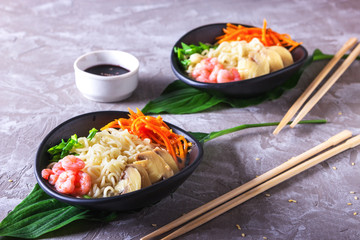 Asian wheat noodles with shrimps, pickled mushrooms, pickled carrots and a scallions in a black plate on green tropical leaves. Asian style, Japanese food'