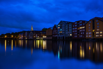 Trondheim cityscape at the blue hour with typical buildings along Nidelva River and the tower bell of Nidaros Cathedral in the background. Trondheim, Norway, August 2018