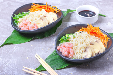 Asian wheat noodles with shrimps, pickled mushrooms, pickled carrots and a scallions in a black plate on green tropical leaves. Asian style, Japanese food'