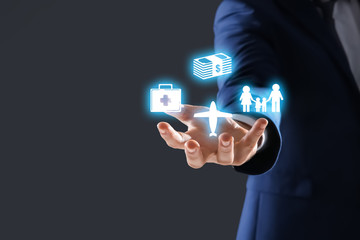 Businessman holding different icons against dark background, space for text. Insurance concept