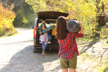 Female camper with sleeping bag near car outdoors. Space for text