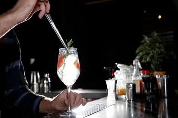Barman making grapefruit gin tonic cocktail at counter in pub, closeup. Space for text