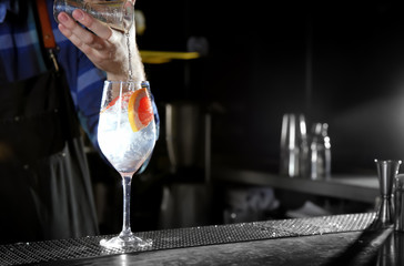 Barman making grapefruit gin tonic cocktail at counter in pub, closeup. Space for text