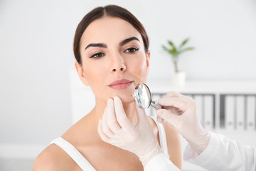 Dermatologist examining young patient's birthmark with magnifying glass in clinic