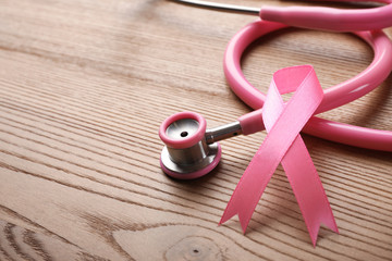 Pink ribbon and stethoscope on wooden background, space for text. Breast cancer concept