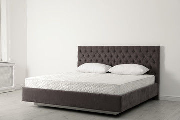 Comfortable bed with new mattress near wall in room. Healthy sleep