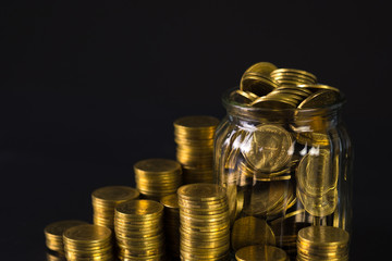 Coins stacks and gold coin money in the glass jar on dark background, for saving for the future banking finance concept.