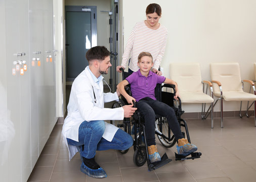 Doctor With Woman And Her Child In Wheelchair At Hospital