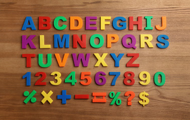 Plastic magnetic letters, numbers and math symbols on wooden background, top view