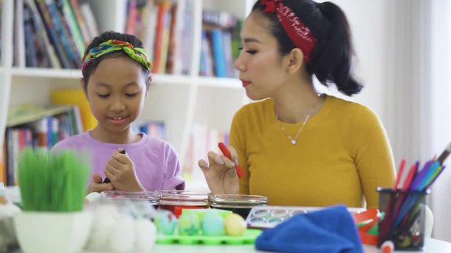 Young woman and her daughter painting easter eggs with dyes and colorful marker on the table at home. Shot in 4k resolution