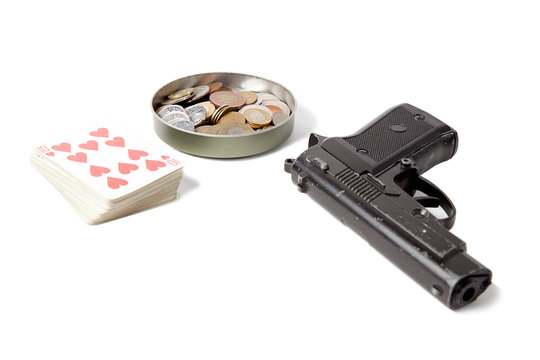 A deck of playing cards, columns of coins from different countries and a black pistol on a white isolated background