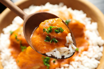 Spoon with tasty butter chicken over bowl of meal, closeup