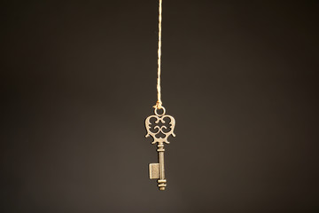 Fototapeta na wymiar Bronze vintage ornate key hanging on thread against dark background