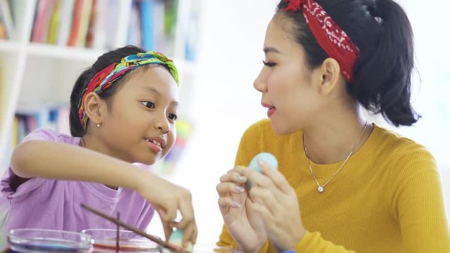 Happy young woman and her daughter painting easter eggs with dyes on the table at home. Shot in 4k resolution
