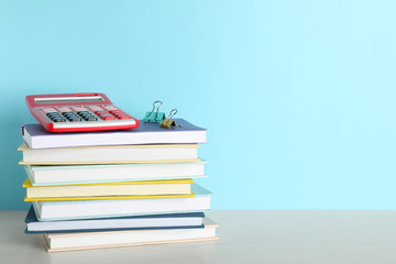 Stack of hardcover books and calculator on table against color background, space for text