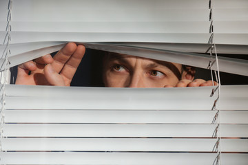 Curious man looking through Venetian window blinds