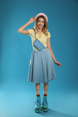 Young woman with retro roller skates on color background