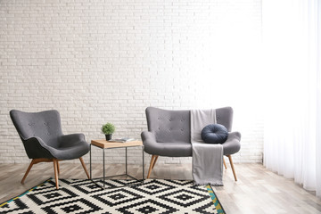 Stylish sofa and armchair near brick wall in modern living room interior. Space for text