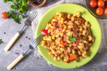 Green plate full of with fresh homemade elbow macaroni pasta , pieces of bell pepper, cherry tomato halves, grated cheese and parsley. Tasty meal