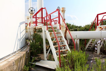 Metal platform with rusted steps surrounded with pipelines and valves at abandoned industrial...