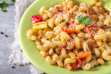 Green plate full of with fresh homemade elbow macaroni pasta , pieces of bell pepper, cherry tomato halves, grated cheese and parsley. Tasty meal